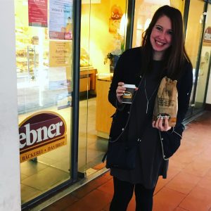 Color picture of brunette Caucasian woman holding paper bag and cup of coffee.